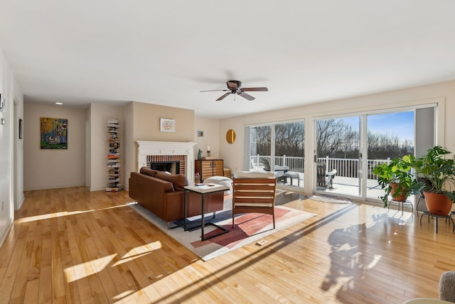 living room with a brick fireplace, light hardwood / wood-style flooring, and ceiling fan