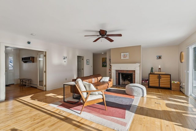 living room with hardwood / wood-style flooring, ceiling fan, a brick fireplace, and baseboard heating