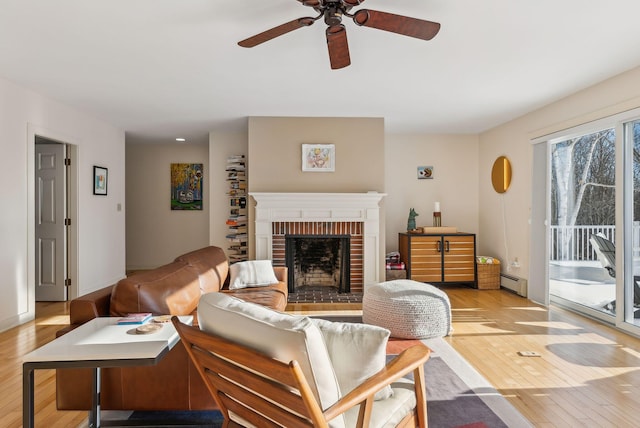 living room featuring light hardwood / wood-style flooring, a fireplace, a baseboard radiator, and ceiling fan