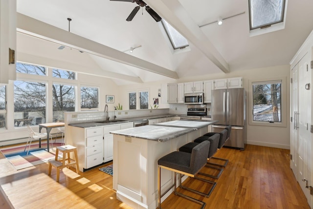 kitchen with sink, lofted ceiling with skylight, stainless steel appliances, a center island, and white cabinets