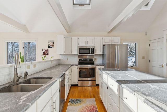 kitchen with lofted ceiling with beams, stainless steel appliances, sink, and white cabinets