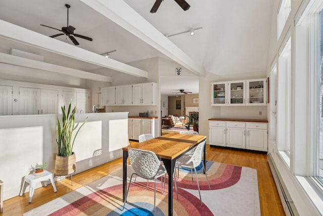 dining room with ceiling fan, a baseboard heating unit, track lighting, vaulted ceiling, and light wood-type flooring