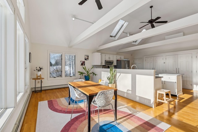 dining space featuring a skylight, high vaulted ceiling, light wood-type flooring, a baseboard radiator, and ceiling fan