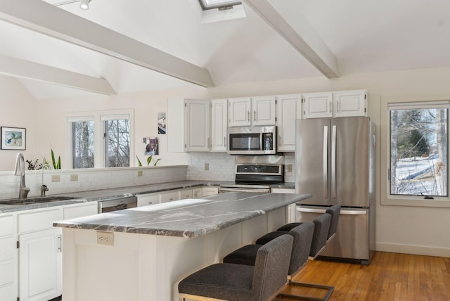 kitchen with sink, appliances with stainless steel finishes, white cabinetry, vaulted ceiling with skylight, and a kitchen bar