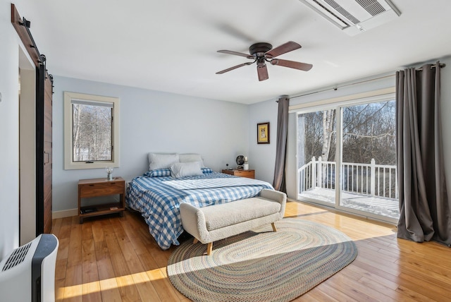 bedroom with light hardwood / wood-style flooring, access to outside, a barn door, and ceiling fan