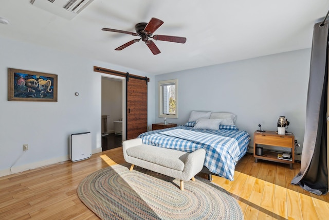 bedroom featuring ceiling fan, a barn door, and light wood-type flooring