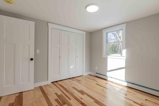 unfurnished bedroom with light hardwood / wood-style floors, a closet, and a baseboard heating unit