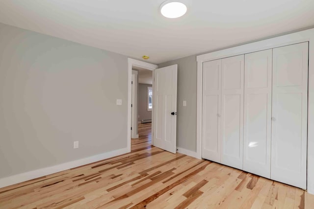 unfurnished bedroom featuring a closet, light hardwood / wood-style floors, and baseboard heating