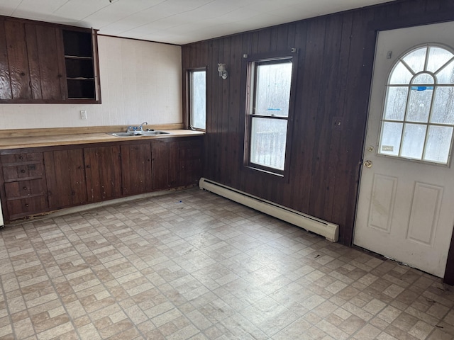 kitchen with dark brown cabinetry, a baseboard radiator, wooden walls, and sink