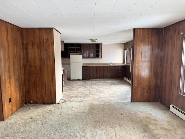 kitchen with dark brown cabinets, baseboard heating, wooden walls, sink, and white fridge