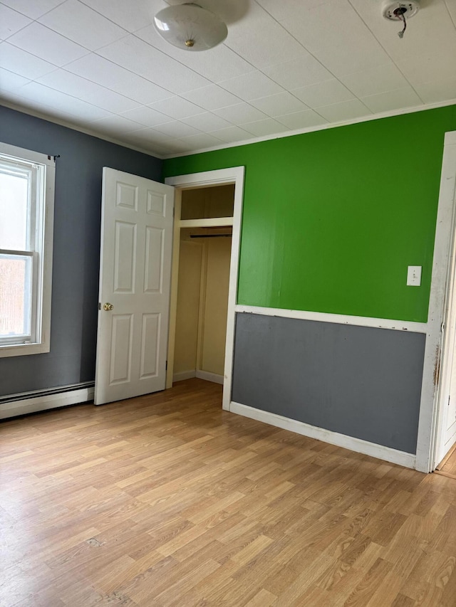 unfurnished bedroom featuring light wood-type flooring, a baseboard radiator, a closet, and crown molding