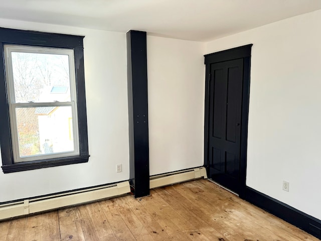 unfurnished room with baseboard heating and light hardwood / wood-style flooring