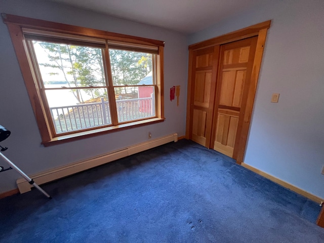 unfurnished bedroom with dark carpet, baseboard heating, and multiple windows