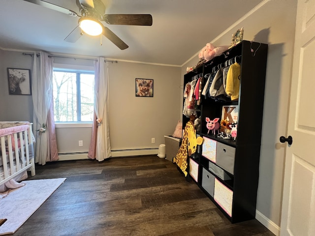 bedroom with ceiling fan, dark wood-type flooring, a baseboard heating unit, crown molding, and a crib