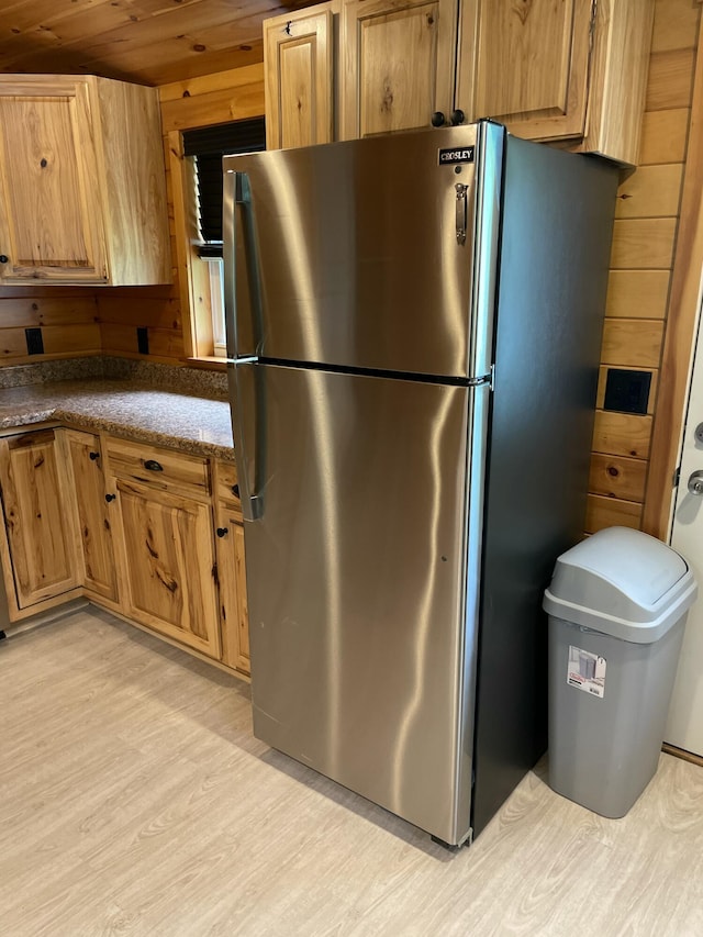 kitchen with stainless steel refrigerator, light hardwood / wood-style flooring, dark stone countertops, wooden walls, and wood ceiling