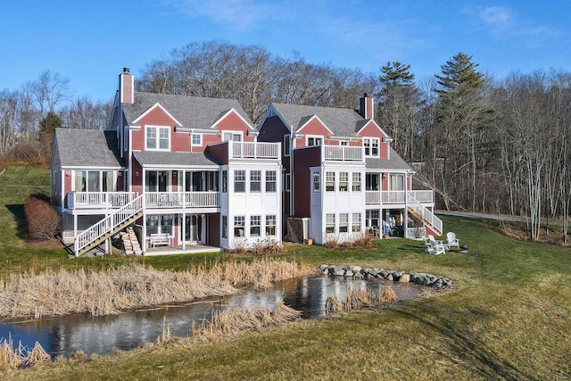 rear view of property featuring a deck with water view, a lawn, and a sunroom