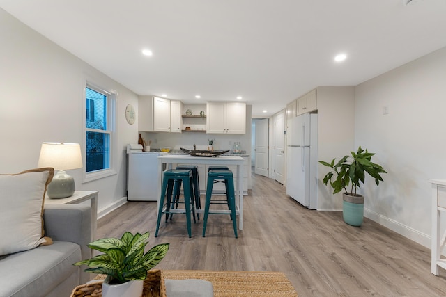 kitchen featuring white refrigerator, light wood-type flooring, white cabinetry, washer / clothes dryer, and a kitchen breakfast bar