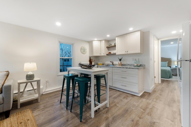 kitchen featuring light stone counters, white cabinetry, fridge, and light wood-type flooring