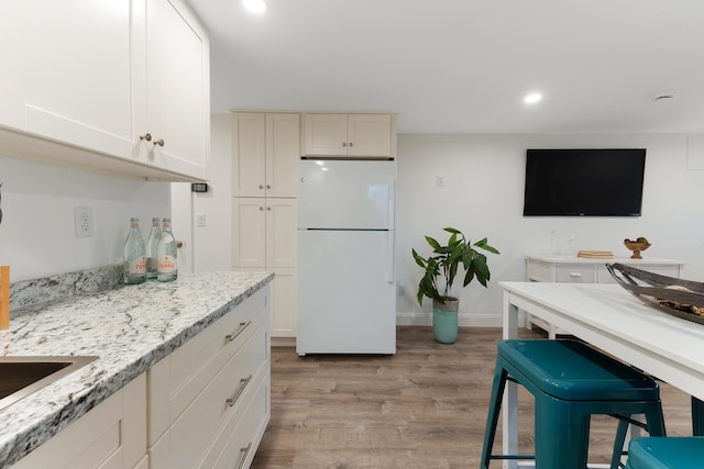 kitchen featuring white refrigerator, light hardwood / wood-style flooring, a kitchen bar, and light stone counters