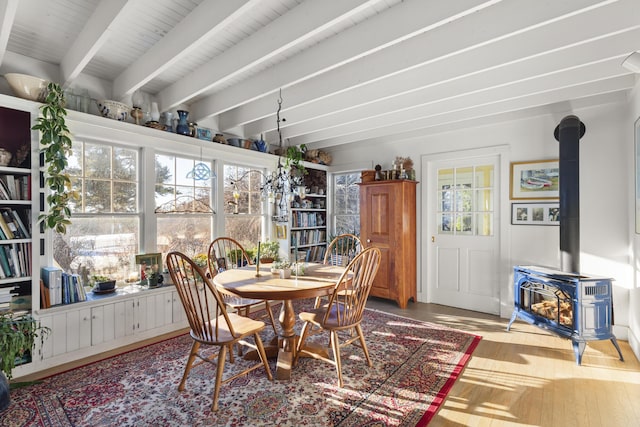 dining area featuring beamed ceiling, a wealth of natural light, hardwood / wood-style flooring, and a wood stove