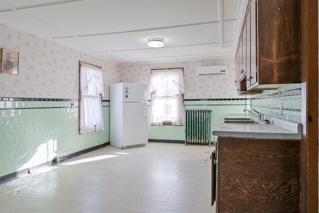 kitchen with radiator, dark brown cabinetry, a wall unit AC, sink, and white refrigerator