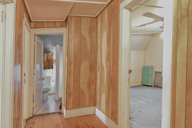 corridor with radiator, wooden walls, light hardwood / wood-style floors, and vaulted ceiling