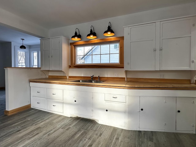 kitchen featuring white cabinetry, sink, hanging light fixtures, and light wood-type flooring