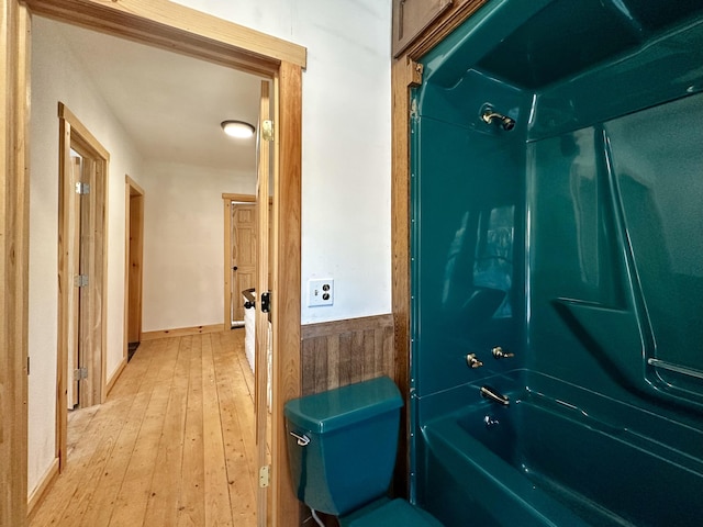 bathroom with hardwood / wood-style flooring, wooden walls, and bathing tub / shower combination