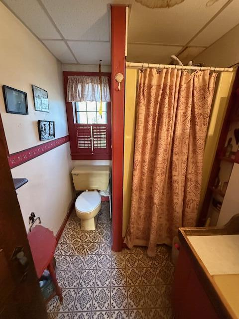 bathroom featuring a paneled ceiling, tile patterned flooring, a shower with shower curtain, and toilet