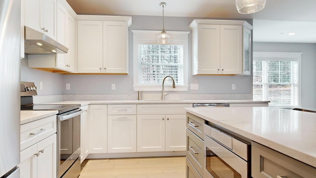 kitchen featuring white cabinets, sink, light wood-type flooring, appliances with stainless steel finishes, and decorative light fixtures