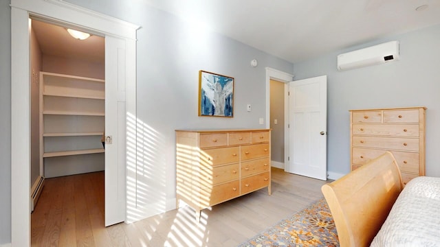 bedroom with a wall mounted AC, a baseboard heating unit, and light wood-type flooring