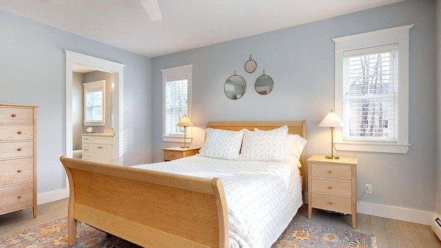 bedroom with hardwood / wood-style floors, ceiling fan, and a baseboard heating unit