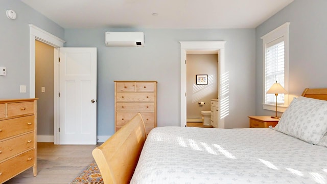 bedroom featuring a wall mounted air conditioner, a baseboard radiator, ensuite bath, and light hardwood / wood-style flooring