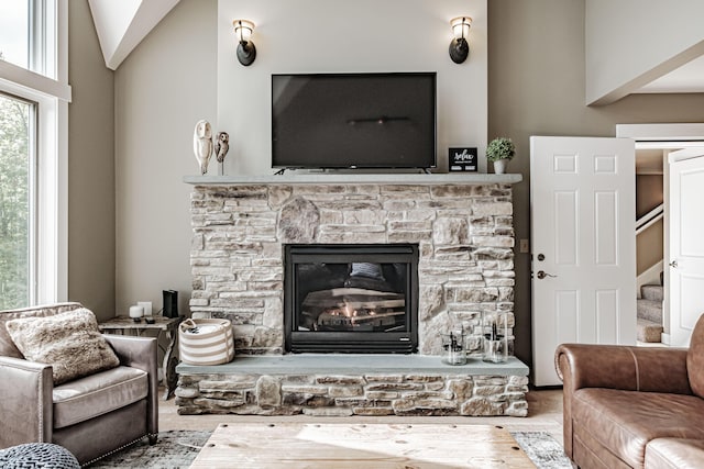 living room featuring a stone fireplace, wood-type flooring, and lofted ceiling