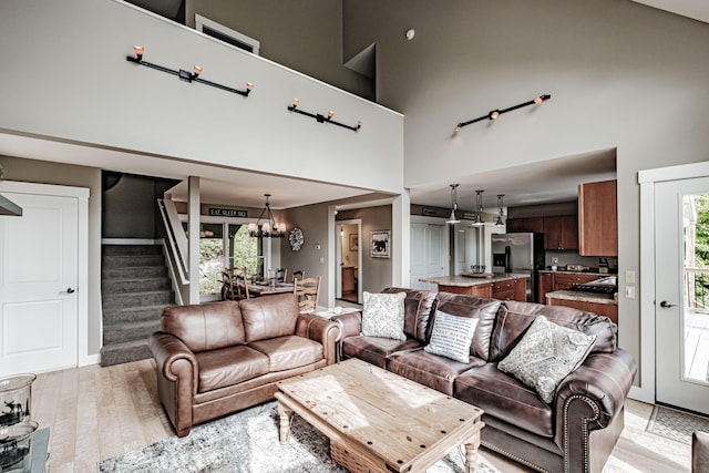 living room with plenty of natural light, a towering ceiling, light wood-type flooring, and an inviting chandelier