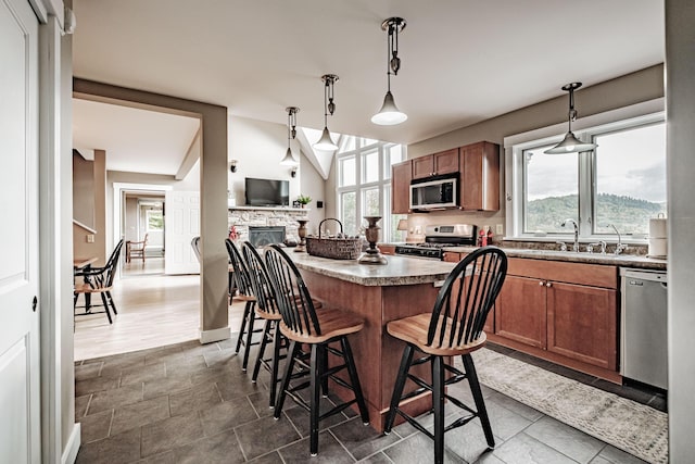 kitchen with a breakfast bar, a stone fireplace, sink, appliances with stainless steel finishes, and decorative light fixtures