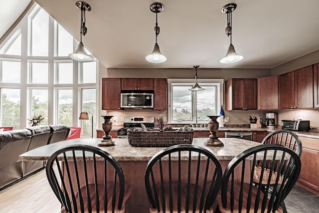 kitchen with light stone counters, hanging light fixtures, stainless steel appliances, and sink