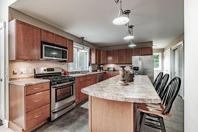 kitchen featuring a center island, sink, hanging light fixtures, stainless steel appliances, and a breakfast bar