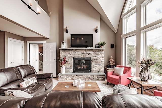 living room with hardwood / wood-style flooring, a healthy amount of sunlight, a stone fireplace, and high vaulted ceiling