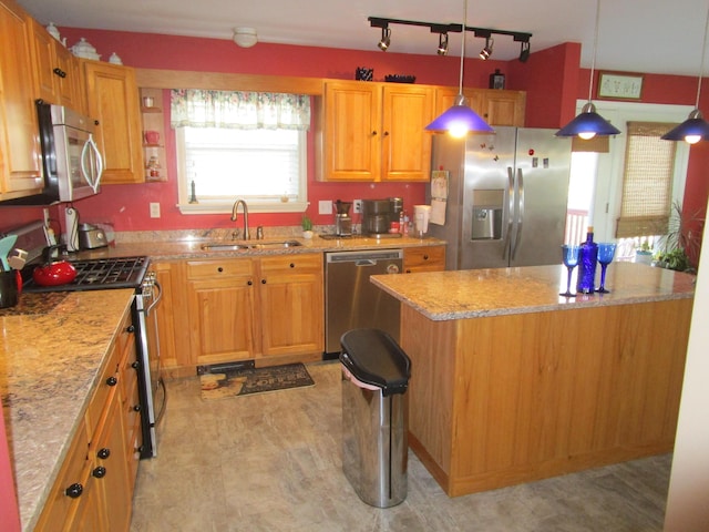 kitchen with light stone countertops, light wood-type flooring, stainless steel appliances, sink, and pendant lighting