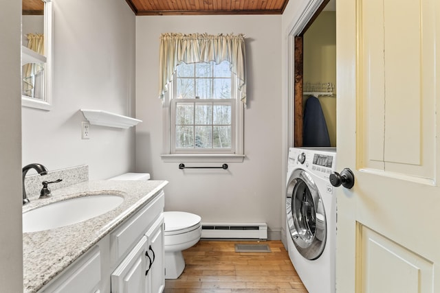 bathroom featuring vanity, baseboard heating, wood-type flooring, washer / clothes dryer, and toilet