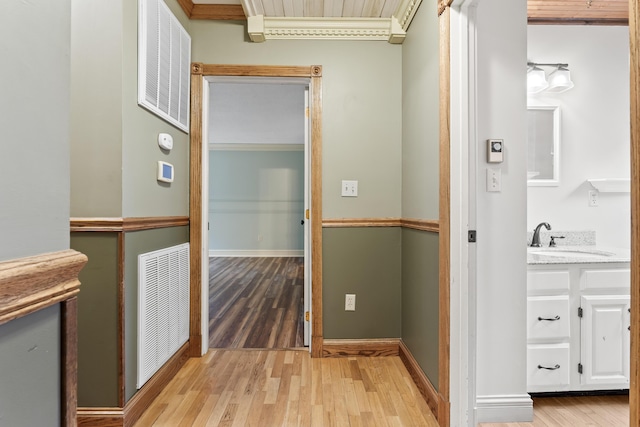 corridor with light hardwood / wood-style flooring, ornamental molding, and sink