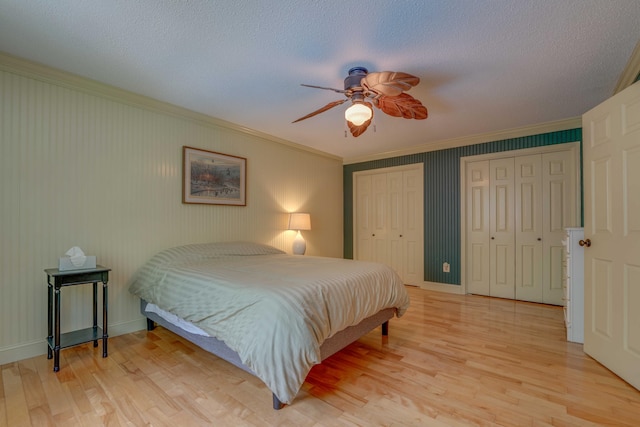 bedroom featuring ceiling fan, light hardwood / wood-style floors, a textured ceiling, two closets, and ornamental molding