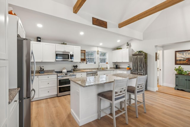 kitchen with a breakfast bar, a center island, light stone countertops, appliances with stainless steel finishes, and white cabinetry