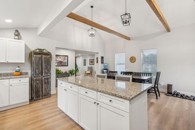 kitchen with light wood-type flooring, pendant lighting, beam ceiling, a center island, and white cabinetry