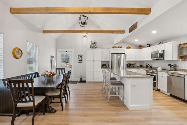 kitchen with beam ceiling, light stone counters, decorative light fixtures, a kitchen island, and appliances with stainless steel finishes