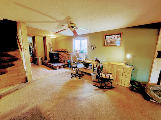 office area with a wood stove, ceiling fan, wood-type flooring, and a textured ceiling