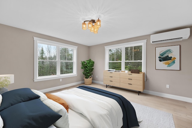 bedroom with a wall mounted AC, a notable chandelier, multiple windows, and light wood-type flooring