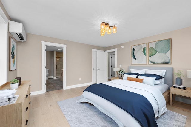 bedroom with an AC wall unit, ensuite bath, an inviting chandelier, and light wood-type flooring