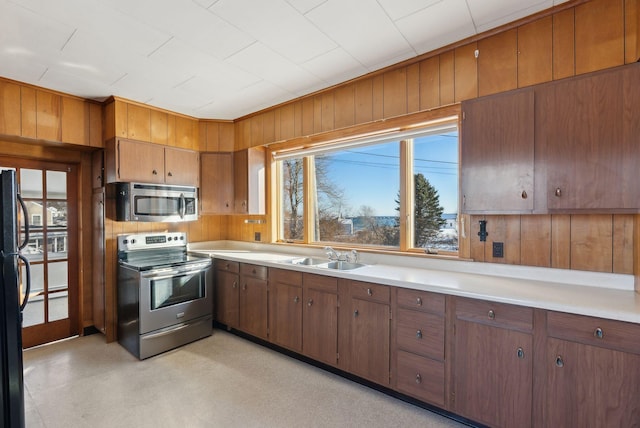 kitchen with wood walls, appliances with stainless steel finishes, light countertops, and a sink